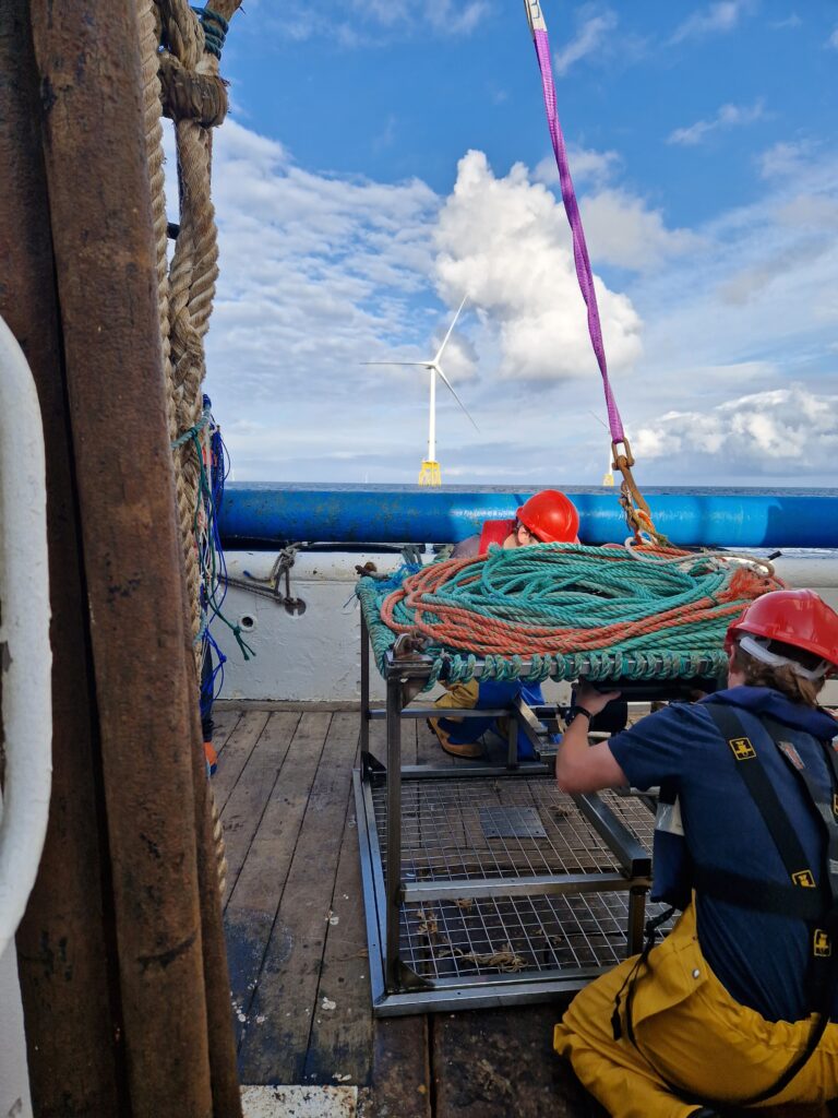 2 PrePARED team members crouching next to BRUV with windfarm in background